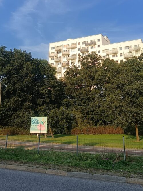 Hochhaus vor blauem Himmel mit Grünstrukturen und Bäumen davor